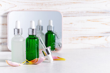 Creative composition with two skin care serums in glass bottles on white rustic background with mirror and pink tulip petals. Skin care concept. Organic cosmetic products.