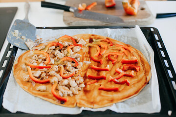 Pizza home made dough with sauce, roasted chicken and pepper on tray in modern kitchen. Home cooking