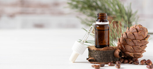 Banner, organic cosmetics concept, glass bottle with oil, pipette and cedar cone on light wooden background