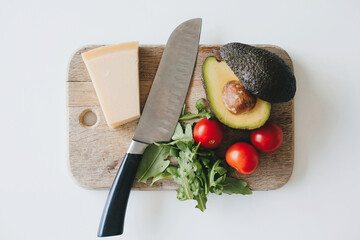 Avocado, cherry tomatoes, arugula, parmesan and knife on wooden cutting board. Healthy eating