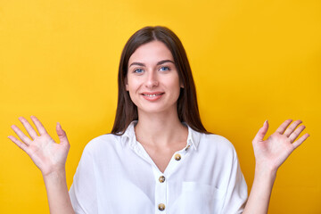 Portrait of brunette girl smiling and shows her palms to the right and left sides isolated on yellow background
