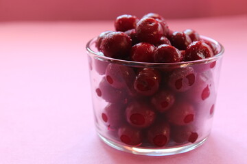 cherry in a glass on a pink red background with a place to text the view from the side close-up of the copyspace
