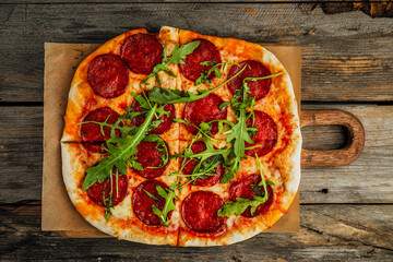 A pepperoni pizza with rocket salad on a wooden board, wooden rustic backdrop