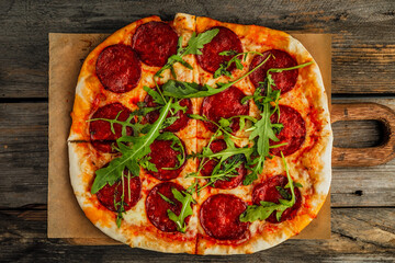 A pepperoni pizza with rocket salad on a wooden board, wooden rustic backdrop