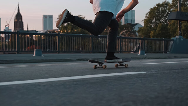 skateboarder pushing on bridge in front frankfurt skyline skyscrapers sunset