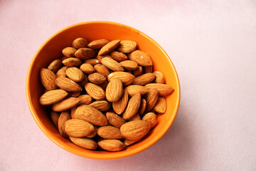 Bowl of fresh almonds on pink color background, top view, healthy fruits bowl 