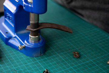 Artisan using hand press for setting snaps in leather for makes a wallet. Hand Pressure Snap Pressing Machine is using by craftsman in leather workshop.