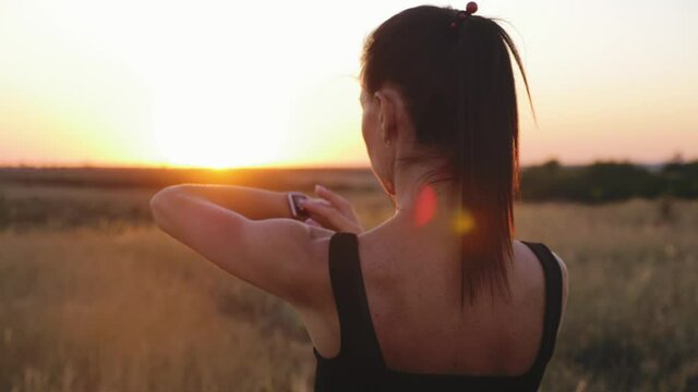 Fit woman use smart watch at sunset. Runner checking pulse on smartwatch on running workout. Modern technology and a healthy lifestyle. Athlete run woman check pulse on fitness bracelet.