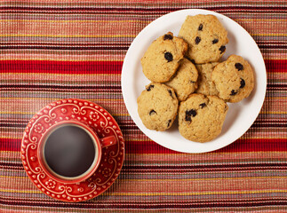 Red cup of coffee with sweet cookies served on a saucer. Overhead photography 