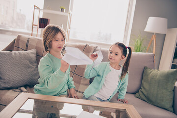 Obraz premium Photo of two positive school persons sit on couch hands hold playing with paper planes have good mood indoors