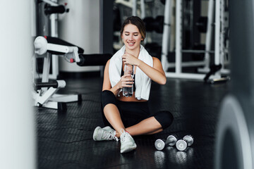 Fototapeta premium Attractive girl with a sports body on the floor in the gym drinks water, workout, lifestyle