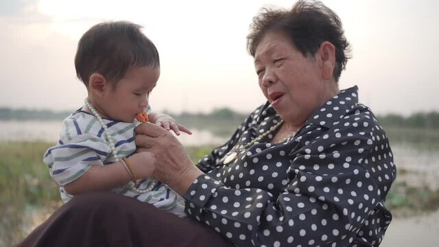 Asian Grandmother and Grandson sitting and playing In Park together in the garden.Happy Asian family conception.
