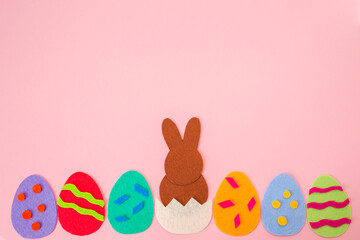 Cut out the felt applications of colorful eggs and brown rabbit hatched from the egg. Pink background. Flat lay. Easter decorations. Copy space
