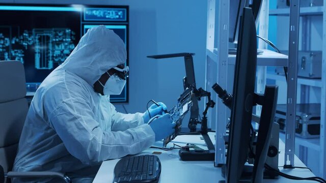 African-american microelectronics engineer works in a modern scientific laboratory on computing systems and microprocessors. Electronic factory worker is testing the motherboard and coding.