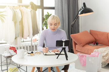 A beautiful pretty girl at home at the table is studying by video conference in the zoom on the phone. A young beauty fashion blogger takes off her vlog and smiles.