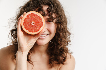 Half-naked curly woman smiling while posing with grapefruit