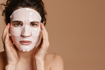 Half-naked woman looking at camera while posing in facial mask