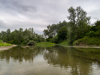Fototapeta na wymiar Landscape with Ukrina river and green riparian zone and underwater weed, natural ecosystem during cloudy summer day