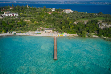 Wooden pier, turquoise water. Panoramic aerial view of Lido delle Bionde beach, Sirmione, Lake Garda, Italy. Island against the blue sky