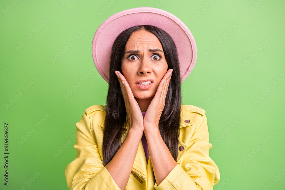 Sticker Photo portrait of nervous stressed woman touching cheekbones hands staring in pink hat isolated on vibrant green color background