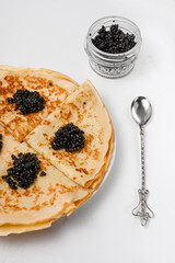 a dish of Russian cuisine: pancakes with black sturgeon caviar on a plate on a white background