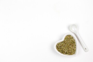 Dried herbs or spices in a bowl with spoon on a white background 