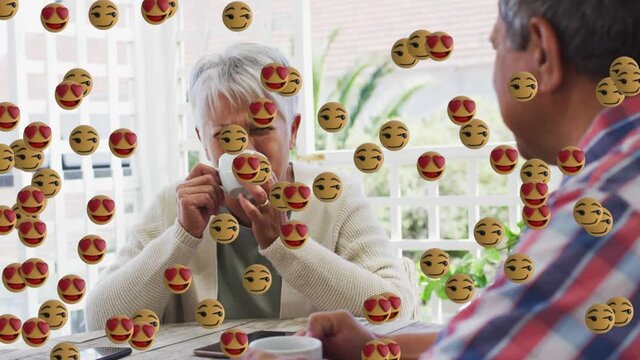 Face emojis floating against african american senior couple drinking coffee together at home