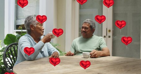 Animation of red hearts over senior couple drinking coffee at home - Powered by Adobe