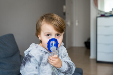 Sick child boy doing inhalation at home, toddler doing therapy aerosol using a nebulizer. Concept...