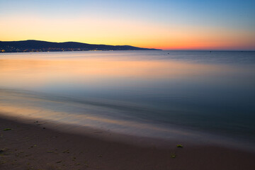 Fototapeta premium Still blue sea water under colorful evening cloudy sky