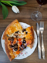 Vegetarian pizza with vegetables on a plate. On the wooden table is a plate of pizza, a glass, and a white tulip flower.