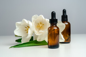 Massage oils in a dark glass jar. Essence for skin health. Trendy style. Mockup for your product. Conceptual photo. 
Aroma Oil and tulips on a white background.