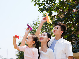 A happy family of three throwing paper airplanes outdoors