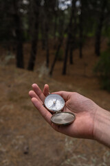 Hand holding a compass in the forest. Concept of exploration and adventure. Vertical shot.