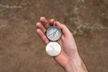 Man's hand holding a compass in the forest. Overhead shot.