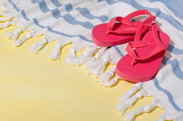 Striped towel and pink flip flops on the bright yellow surface.Empty space