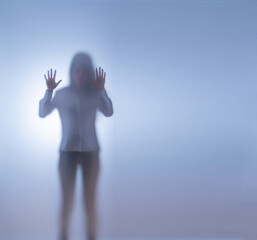 A young woman stands behind frosted glass. The concept of kidnapping and keeping them in captivity