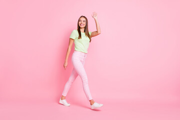 Fototapeta na wymiar Full length photo of cute pretty young girl dressed green t-shirt walking waving arm bye isolated pastel pink color background