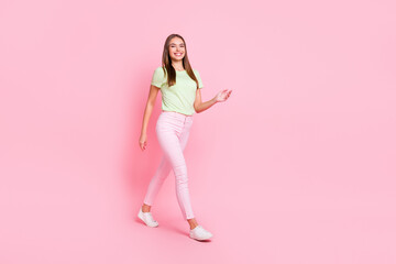 Fototapeta na wymiar Full length photo of funny sweet young lady wear green t-shirt walking isolated pastel pink color background