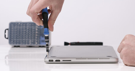 Service worker repairing laptop with magnetic screwdriver tool in white walled lab