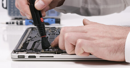 Service worker repairing cleaning dust laptop motherboard circuit board cooler with brush in white...