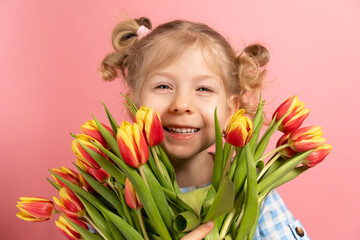 Obraz na płótnie Canvas a small blonde on a pink background with a bouquet of red tulips in her hands, smiling. close-up portrait. holiday concept