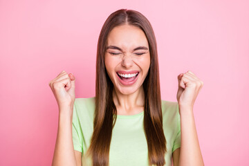 Photo of impressed lucky young lady wear green t-shirt rising fists closed eyes isolated pastel pink color background