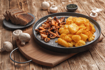 Mushrooms and fried potatoes lie on a concrete plate on a wooden table near raw mushrooms and slices of bread