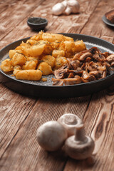 Fried potatoes with mushrooms on a wooden rustic table near fresh mushrooms