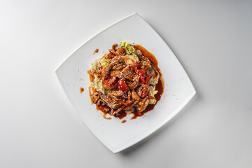 Warm salad with roast pork on a white square plate top view.