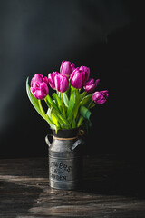 Lilac purple tulip flowers on table. Spring bouquet flowers in vintage vase. Floral concept. Floral background. Dark black background.