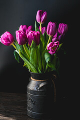 Lilac purple tulip flowers on table. Spring bouquet flowers in vintage vase. Floral concept. Floral background. Dark black background.