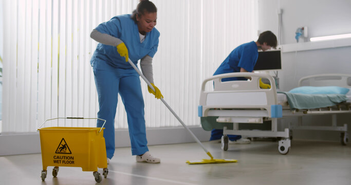 Diverse team of nurses washing floor and changing bed in hospital ward