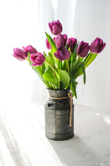 Lilac purple tulip flowers on table. Spring bouquet flowers in vintage vase. Floral concept. Floral background.  White decoration and light background
